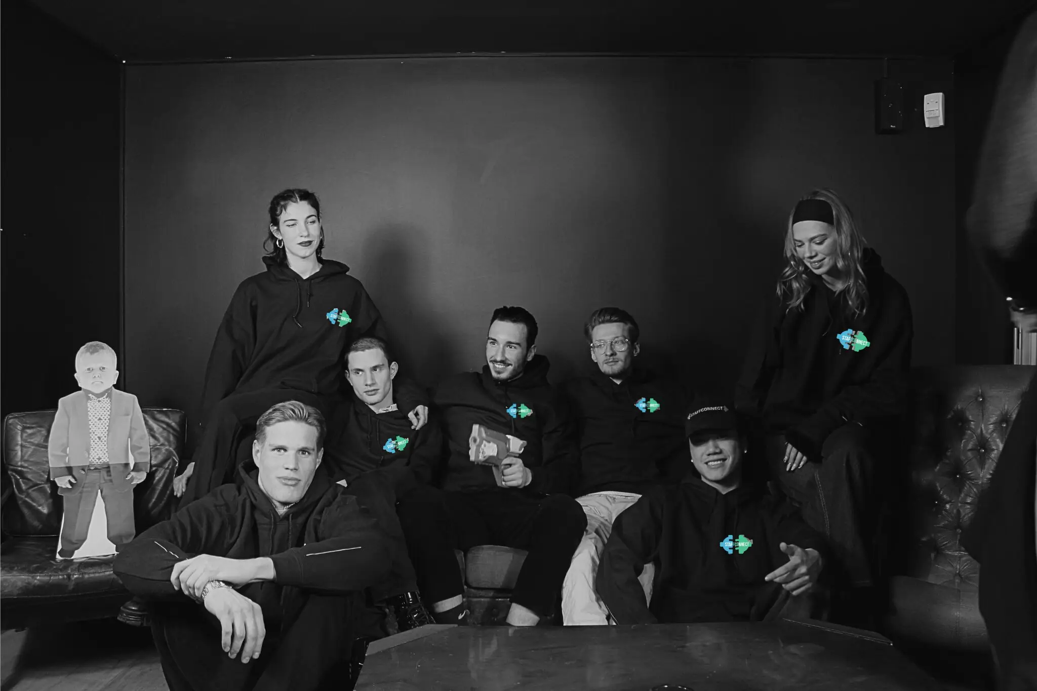 Black-and-white photo: the StaffConnect team in black hoodies on a leather sofa, only the logos on the hoodies in colour