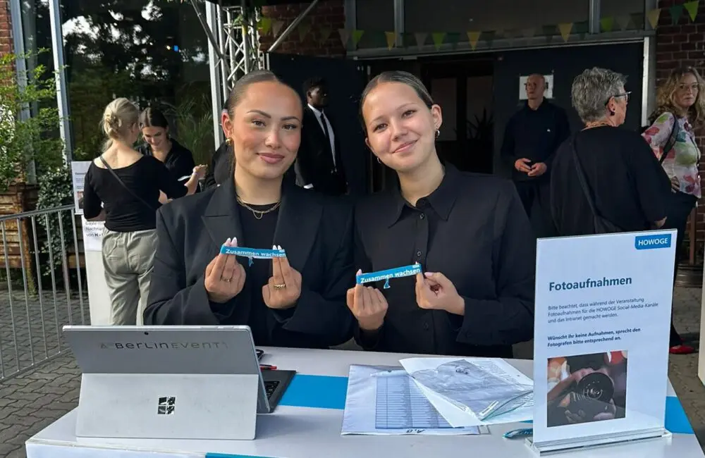 Two staff members at the accreditation desk holding up admission wristbands