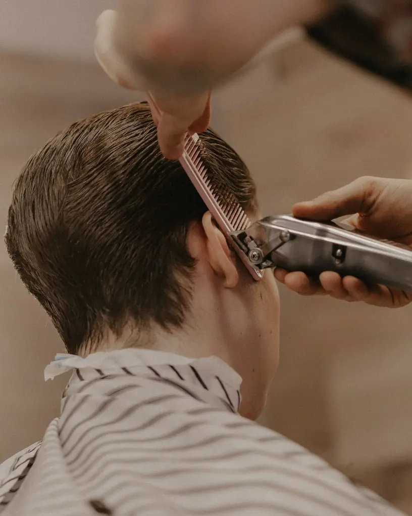 Barber führt die Haarschneidemaschine über dem Kamm und schneidet die Seite über dem Ohr nach – Barber auf Festivals in Berlin