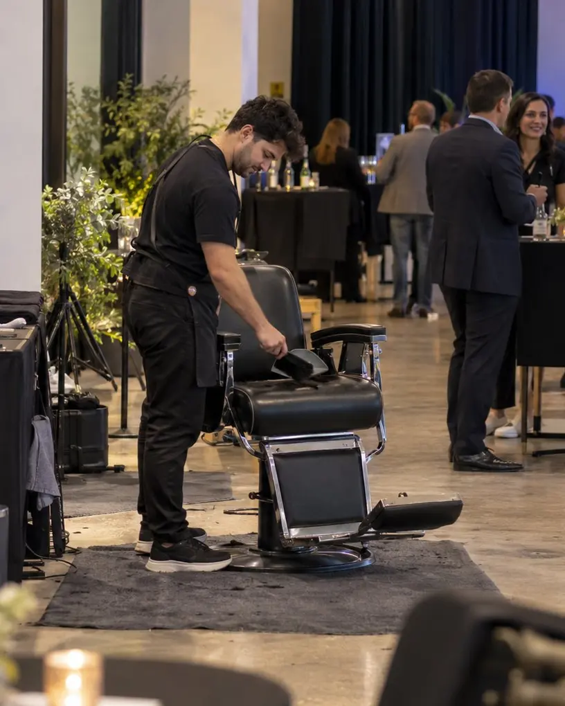 Barber säubert zwischen zwei Gästen den Barberstuhl an seiner Station auf einem Firmenevent – Event-Friseur auf Messe und Kongress