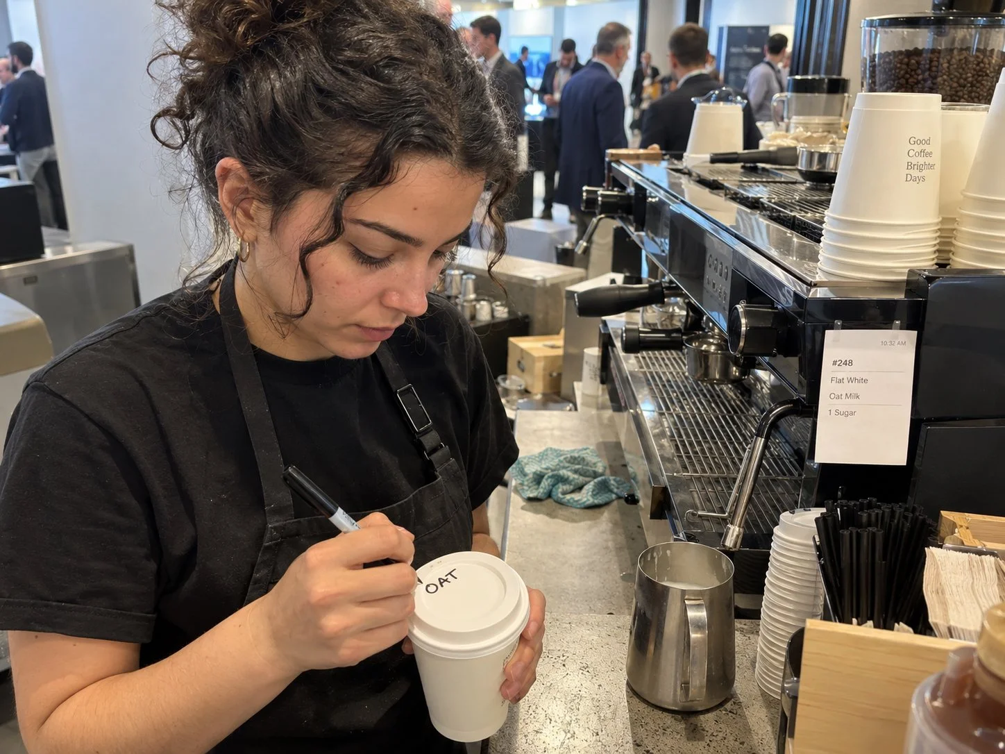 Barista beschriftet an der Kaffeebar einer Konferenz einen Becher für den Flat White mit Hafermilch