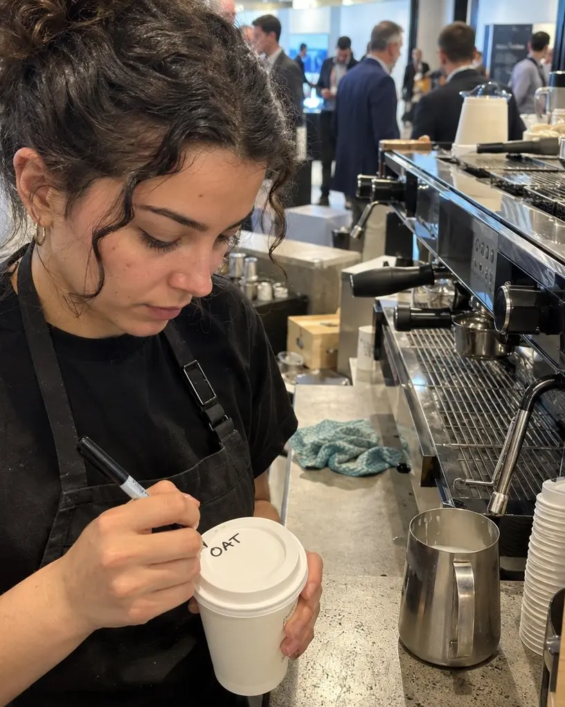 Barista labels a cup for an oat flat white at a coffee bar