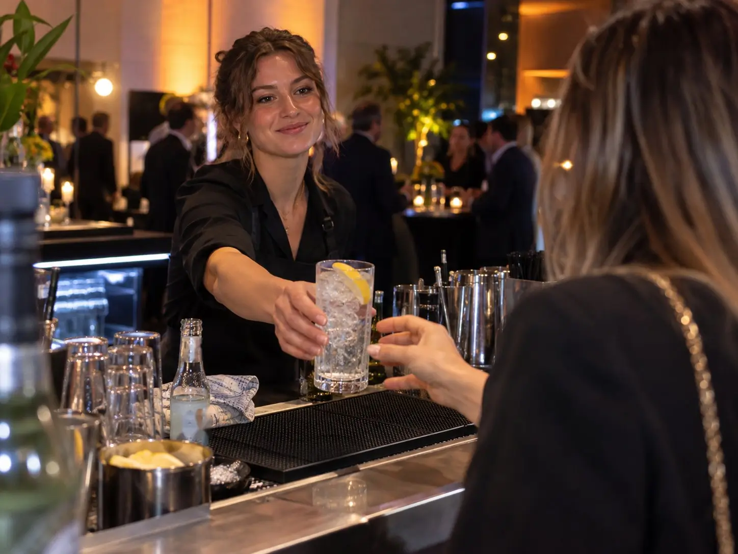 Barkeeperin reicht einem Gast bei einem Abendempfang einen Longdrink über die Theke