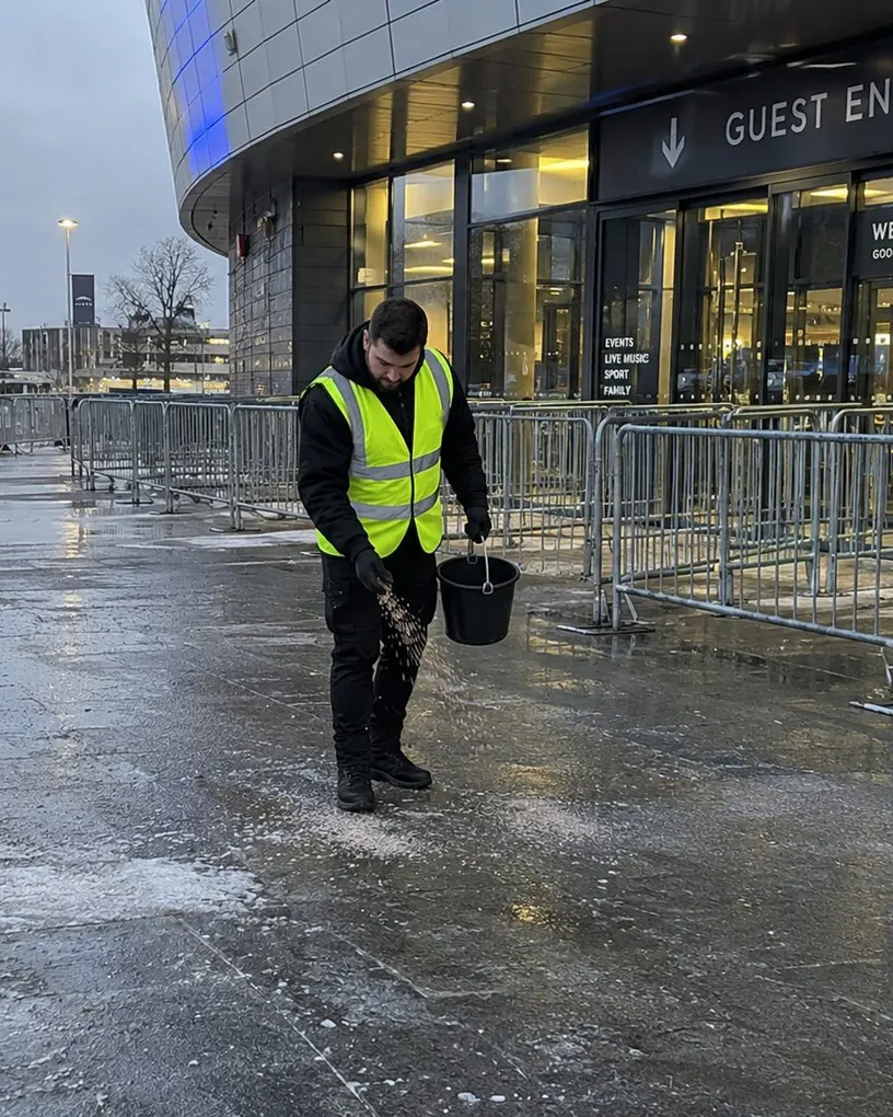 Event helper spreads grit at a guest entrance in winter