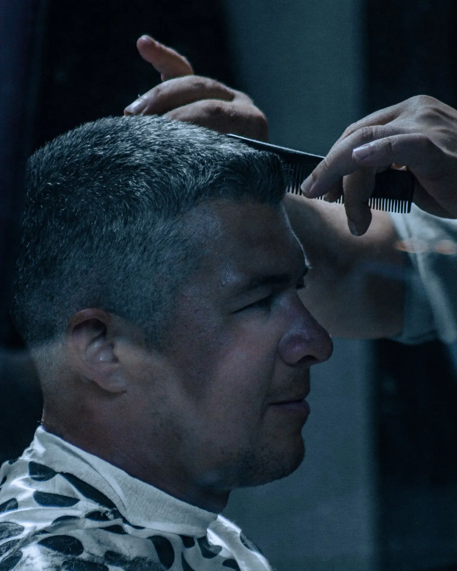 Friseur kämmt einem Gast im Frisierumhang vor dem Auftritt das graue Kurzhaar in Form – Styling backstage