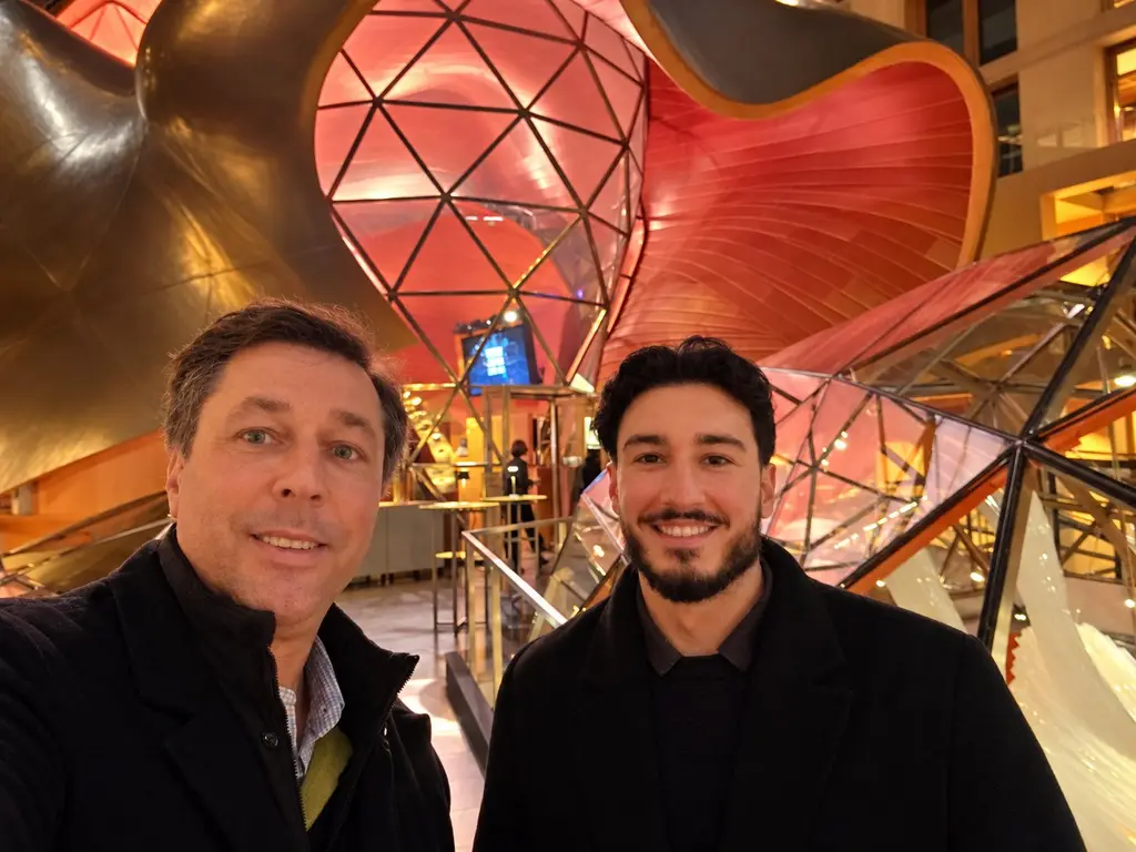 Selfie von Leon Chiosea (rechts) und einem Geschäftspartner vor einer geschwungenen, rot beleuchteten Architektur