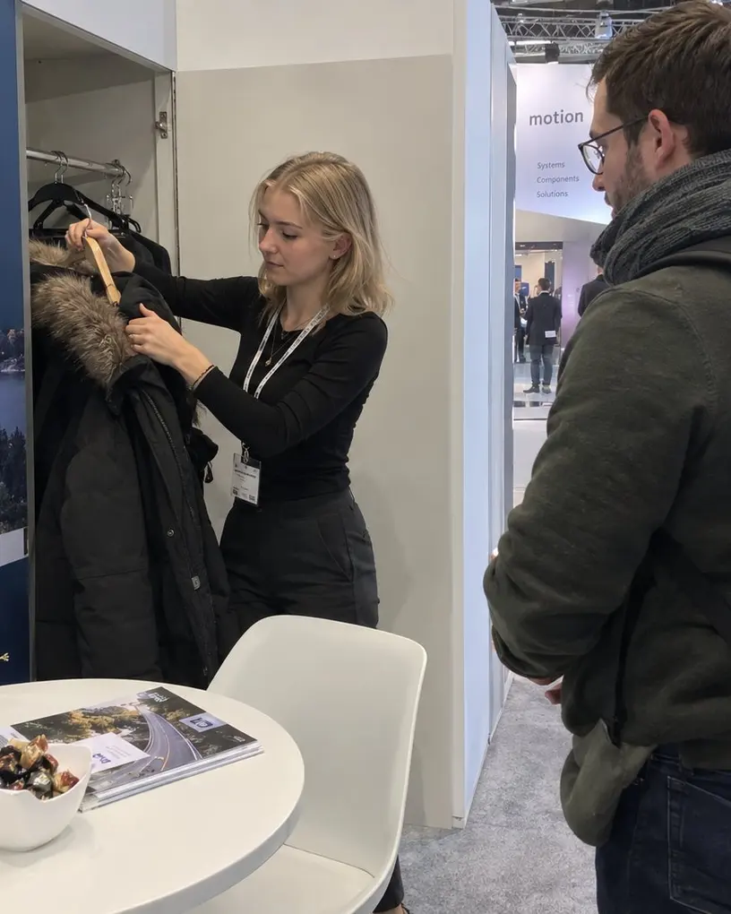 Stand hostess hangs up a visitor’s coat at a trade fair stand