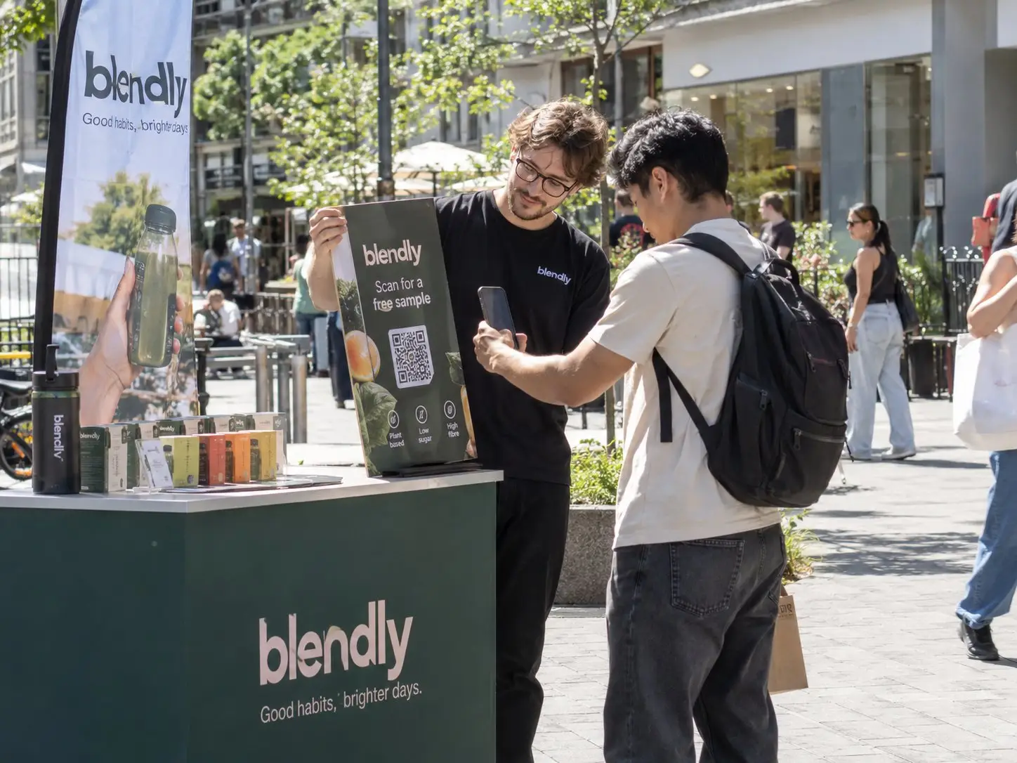 Promoter shows a passer-by the QR code for a free sample at a sampling stand