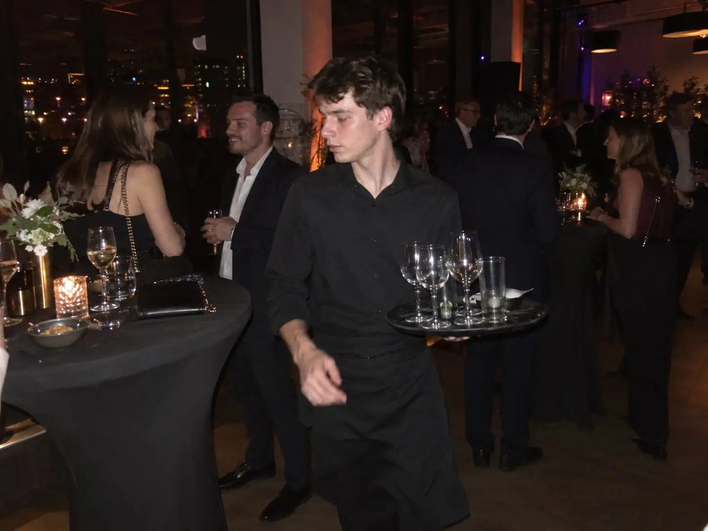Server in black clearing empty glasses onto a tray at an evening reception