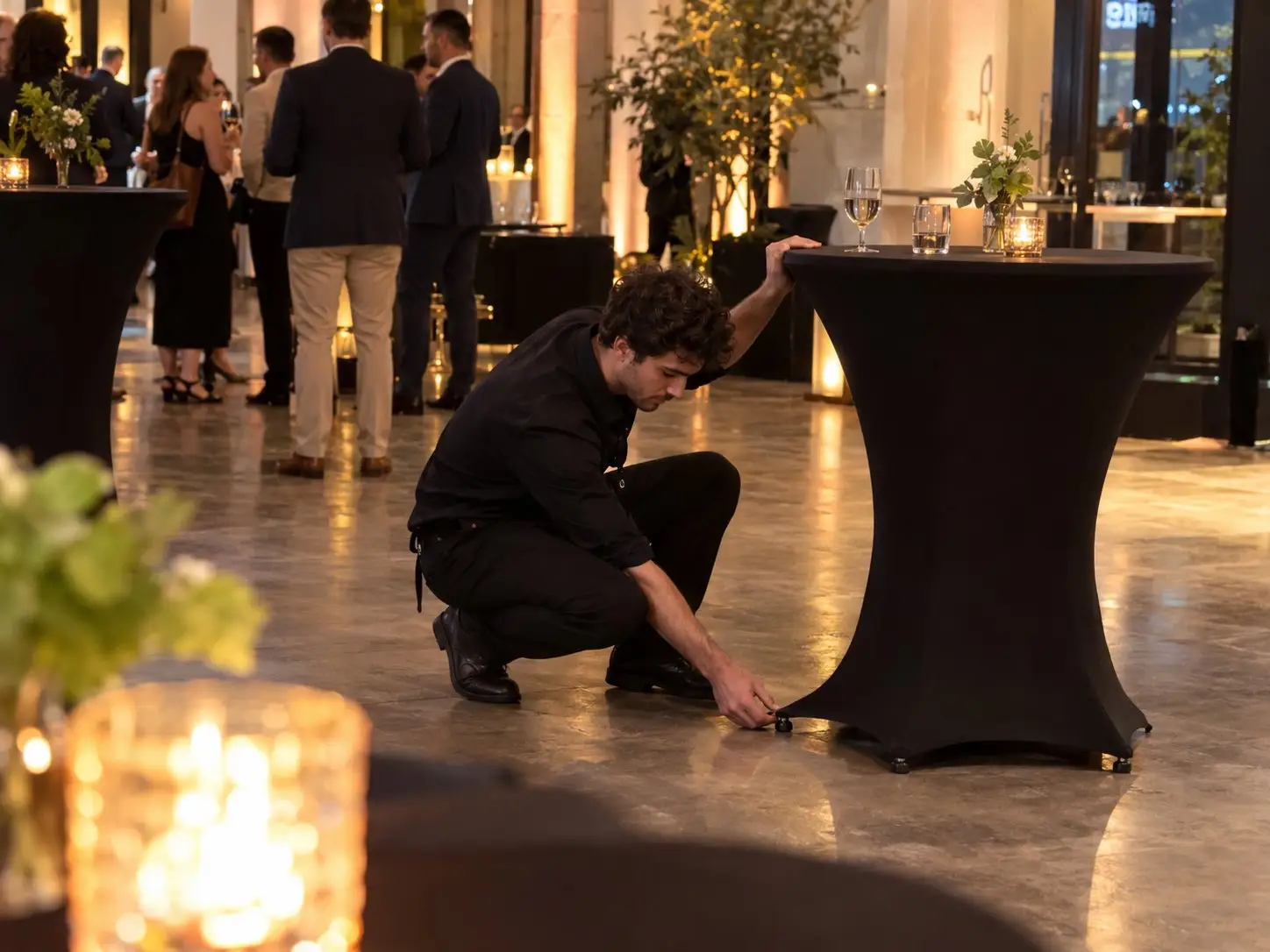 Event helper adjusts a cocktail table before an evening reception