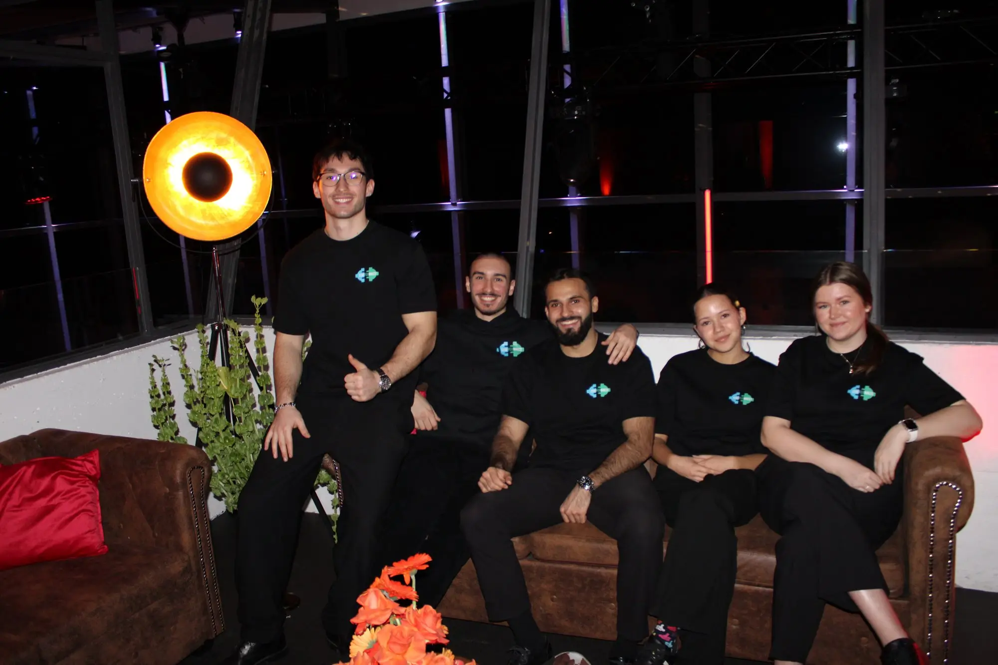 The StaffConnect team in black logo shirts on a Chesterfield sofa in the AVUS grandstand