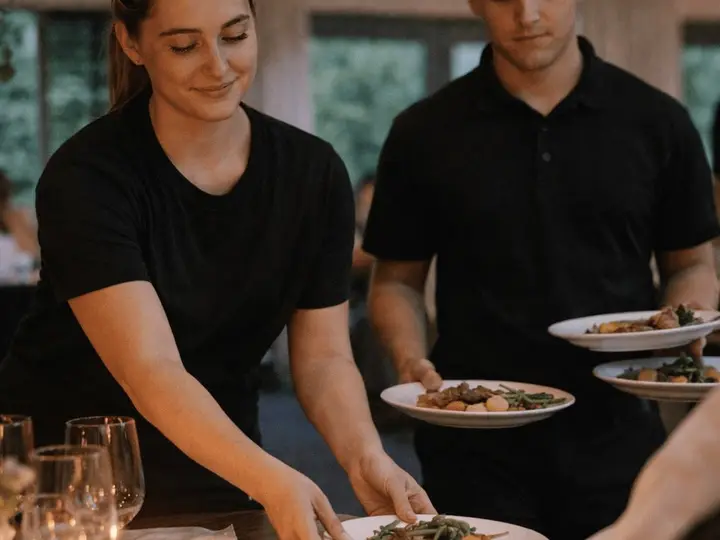 Two waiting staff serving plates at a fully laid banquet table